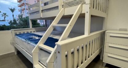 Litera de madera blanca de dos pisos en exposición de Madera y Mar en La Manga del Mar Menor, con vistas a edificios desde la ventana del local