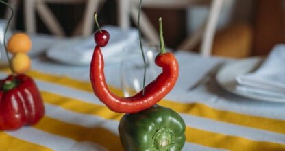 Decoración de mesa creativa en MaracaStudio con pimiento verde, guindilla roja y clavel formando una composición artística sobre mantel de rayas amarillas