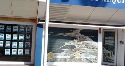 Escaparate de Marítima Inmobiliaria con rótulo azul de venta y alquiler y fotografía aérea del litoral en el cristal