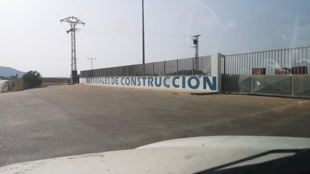 Muro exterior con letrero Materiales de Construcción Simón Sáez junto a valla metálica y zona de almacén