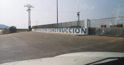 Muro exterior con letrero Materiales de Construcción Simón Sáez junto a valla metálica y zona de almacén