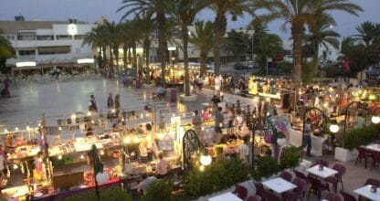 Puestos iluminados y ambiente festivo del Mercadillo Nocturno de La Manga entre palmeras al atardecer