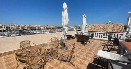 Terraza de azotea con vistas al puerto deportivo de Cabo de Palos, veleros y edificios, mesas de ratán y sombrillas blancas