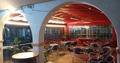 Salón interior de Mesón Los Amigos en La Manga del Mar Menor con arco blanco, barrica de madera y terraza cubierta roja