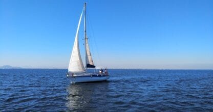 Velero blanco con velas desplegadas navegando en aguas tranquilas y cielo despejado con Milenium Charter en La Manga del Mar Menor