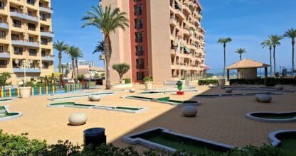 Campo de minigolf con palmeras y edificios de apartamentos al fondo junto al mar en La Manga del Mar Menor