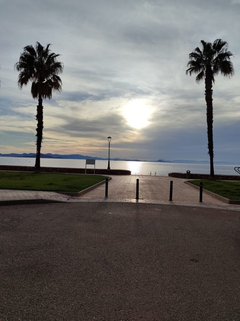 Paseo marítimo al atardecer con dos palmeras enmarcando la vista del Mar Menor desde el Mirador de La Manga