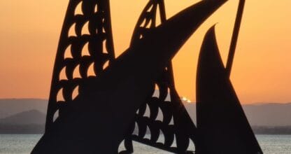 Monumento Velámenes en silueta al atardecer con escultura metálica de velas sobre el Mar Menor en La Manga del Mar Menor