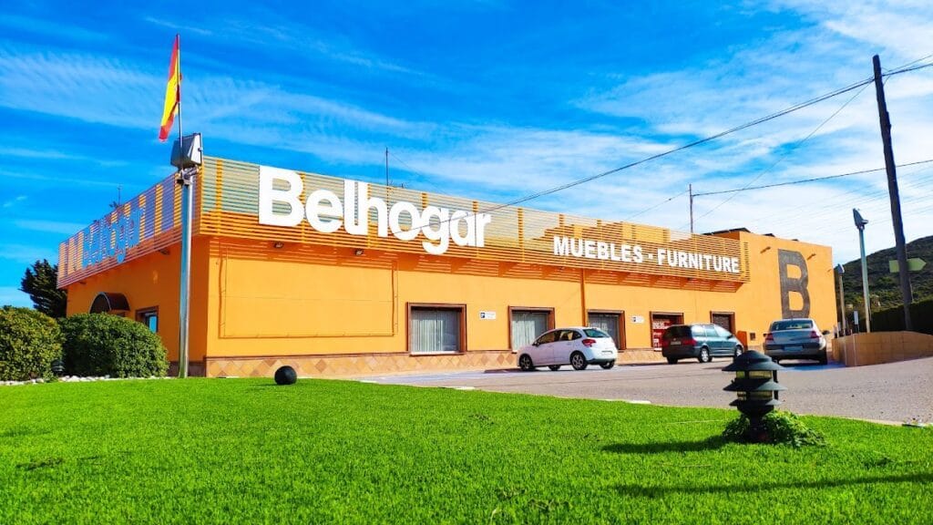 Edificio naranja de gran formato de Muebles Belhogar con rótulo Muebles-Furniture y bandera española en La Manga del Mar Menor