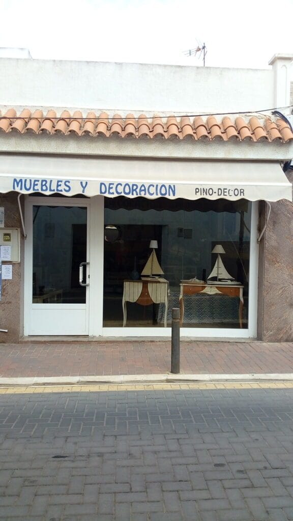 Escaparate de Muebles y Decoración Pino Decor en La Manga del Mar Menor con mesas antiguas, lámparas y maquetas de veleros decorativas