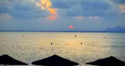 Atardecer sobre el Mar Menor desde la playa de Mundo Activo con sombrillas en silueta y bañistas en el agua