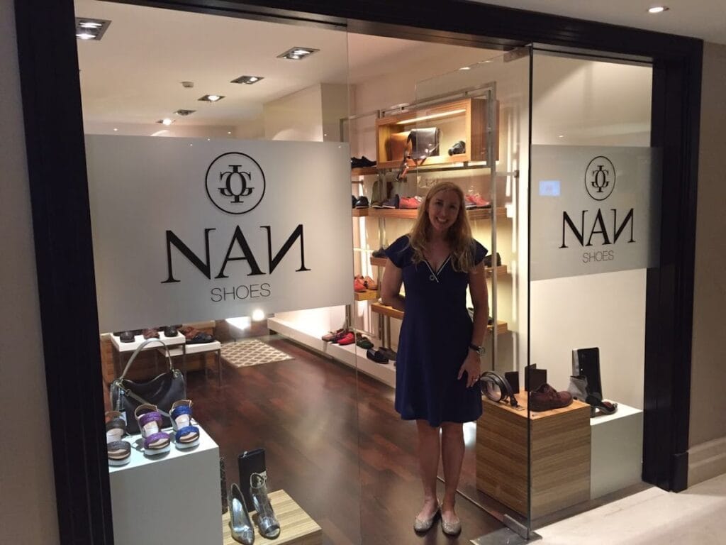 Interior de la tienda NAN Shoes con estanterías iluminadas de calzado y mujer en la entrada, La Manga del Mar Menor