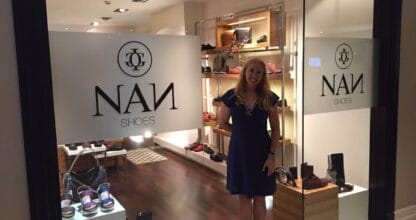 Interior de la tienda NAN Shoes con estanterías iluminadas de calzado y mujer en la entrada, La Manga del Mar Menor