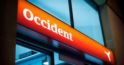 Rótulo luminoso naranja de la agencia de seguros Occident con logo corporativo en blanco sobre fachada de cristal