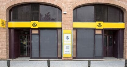 Fachada de oficina de Correos con rótulos amarillos y logo corporativo en edificio de ladrillo visto con doble acceso