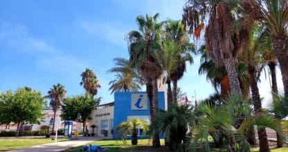Oficina de Turismo de Cabo de Palos rodeada de palmeras, edificio azul con símbolo de información turística
