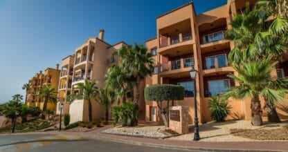 Fachada exterior de apartamentos Ona Lomas Village en La Manga Club con palmeras, balcones y jardines en tonos ocre mediterráneos