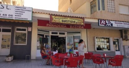 Terraza exterior de Panadería Bastida en La Manga del Mar Menor con mesas y sillas rojas y clientes disfrutando