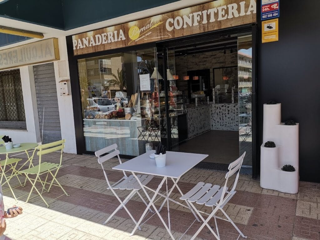 Terraza exterior de Panadería Bernal Confitería en La Manga del Mar Menor con mesas y sillas blancas y escaparate de repostería