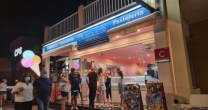 Exterior nocturno de Busquets Cafetería-Heladería en Cabo de Palos con cola de clientes, rótulo azul de pastelería y helados y logo desde 1968