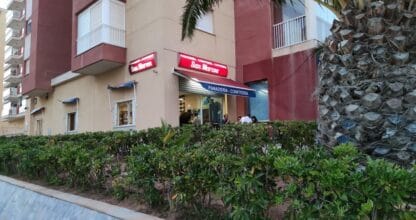 Fachada con rótulos luminosos rojos de Panadería Confitería San Marcos con clientes en el interior, La Manga del Mar Menor