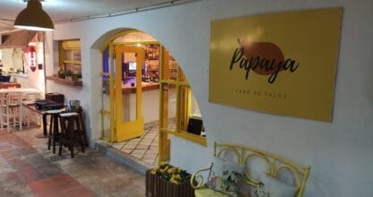 Entrada al restaurante Papaya en Cabo de Palos con arco amarillo, cartel corporativo y banco decorativo en la terraza