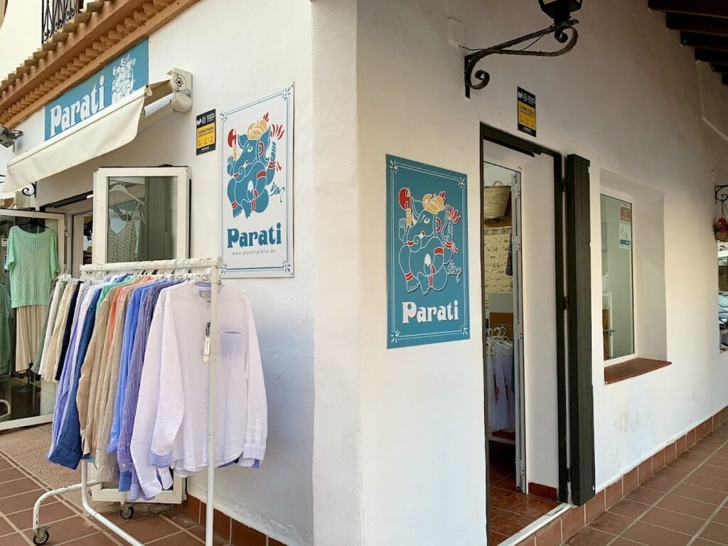 Fachada de Parati Plata La Manga con perchero de camisas de colores y carteles con logo de elefante azul en patio andaluz
