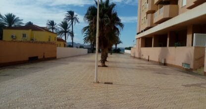 Plaza peatonal con palmeras y adoquines junto a edificio residencial en La Manga del Mar Menor con vistas al mar al fondo