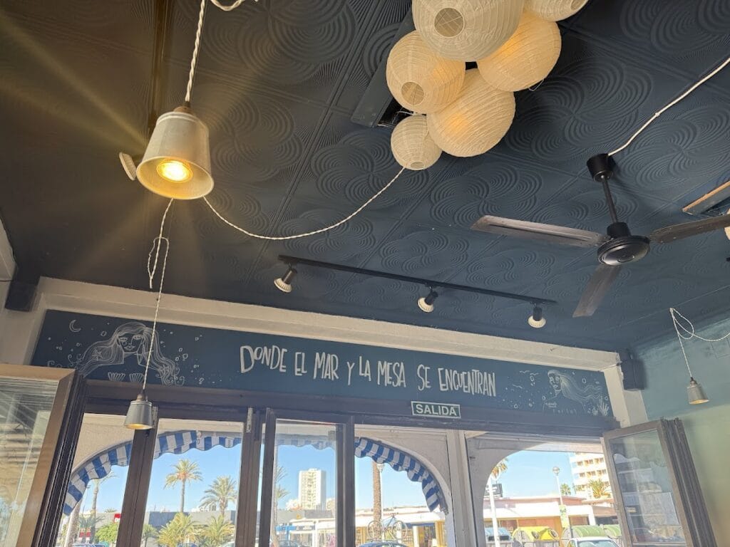 Interior de Patapalo tapas con techo oscuro, farolillos de papel y mural que reza donde el mar y la mesa se encuentran