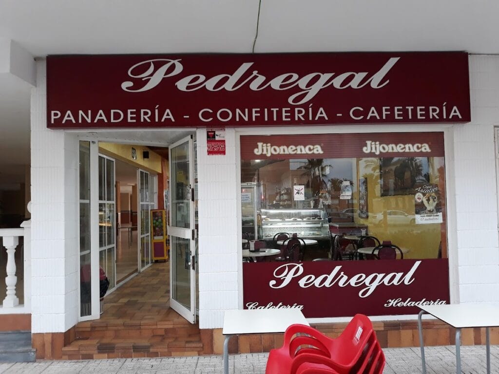 Fachada del Pedregal Cafetería Confitería Heladería en La Manga con gran rótulo granate, logo Jijonenca en escaparate y sillas rojas en la acera