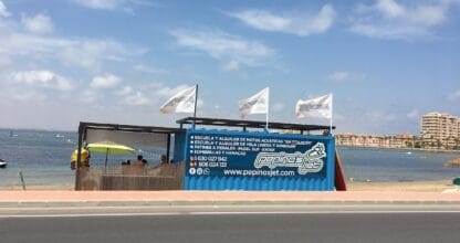 Puesto de Pepino's Jet en la orilla del Mar Menor con bandera y cartel azul de alquiler de motos acuáticas, kayak y windsurf