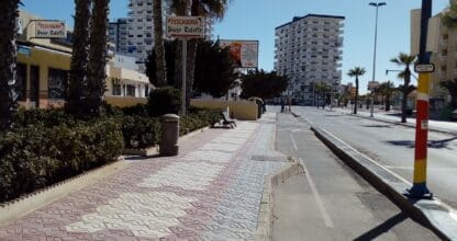 Avenida peatonal de La Manga del Mar Menor con palmeras y cartel de Pescadería Diego Rebollo visible entre la vegetación junto a la calzada