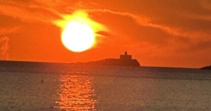 Espectacular puesta de sol naranja sobre el mar con silueta de islote y faro, vista desde Pescados Cabomar en Cabo de Palos
