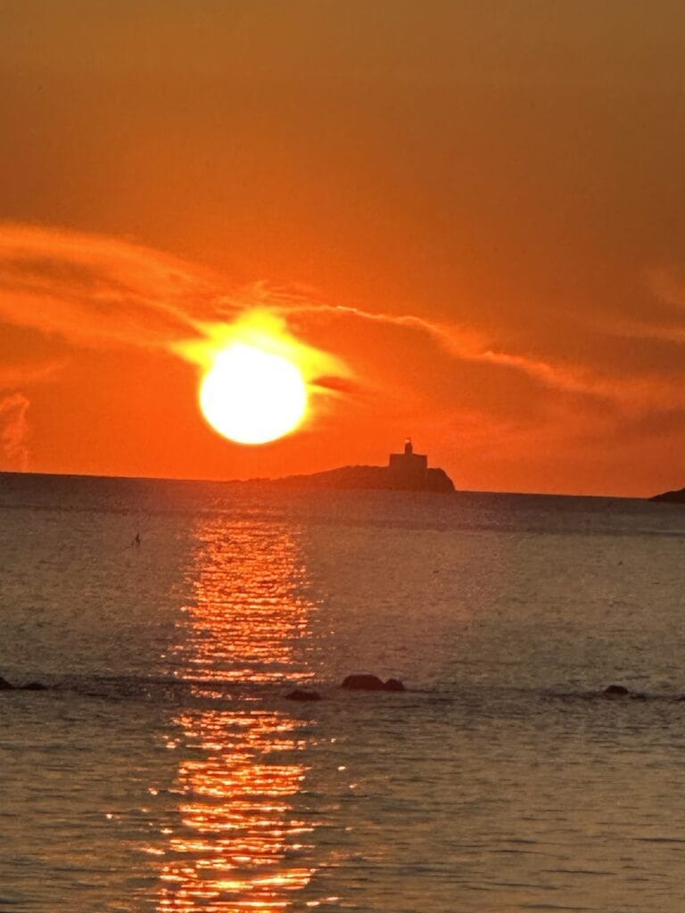 Espectacular puesta de sol naranja sobre el mar con silueta de islote y faro, vista desde Pescados Cabomar en Cabo de Palos