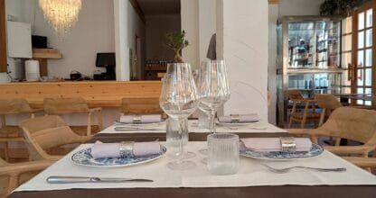 Mesa preparada en Pezio con vajilla azul y blanca, copas de cristal acanalado y araña de lámpara sobre sala de madera natural