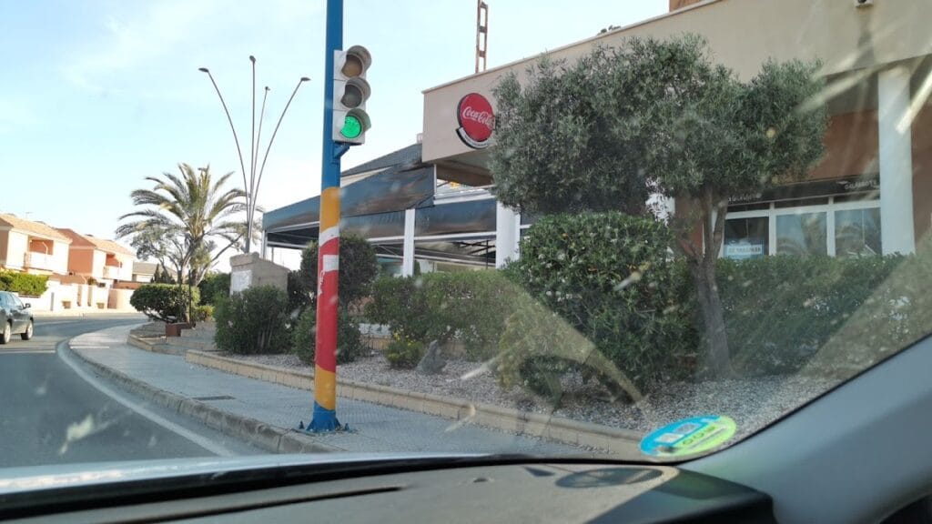 Vista exterior desde el coche de Pizzeria Las Dunas con semáforo en verde y palmeras en La Manga del Mar Menor