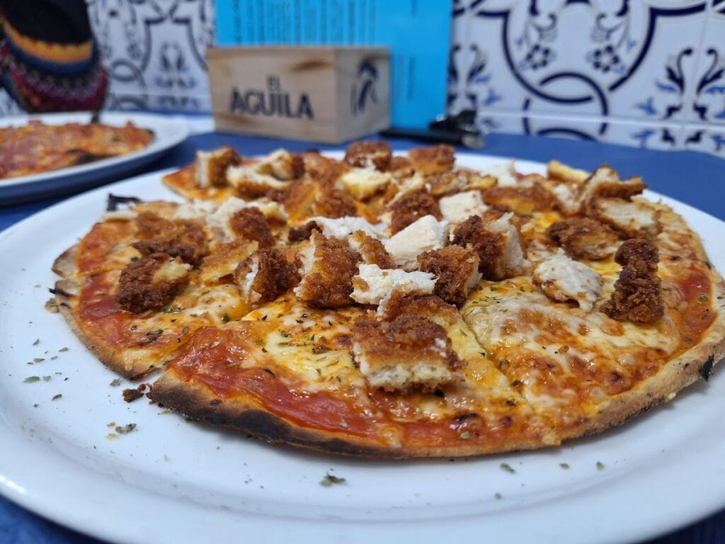Pizza con pollo crujiente empanado y queso fundido sobre plato blanco en Pizzería Los Primos, La Manga del Mar Menor