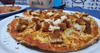 Pizza con pollo crujiente empanado y queso fundido sobre plato blanco en Pizzería Los Primos, La Manga del Mar Menor
