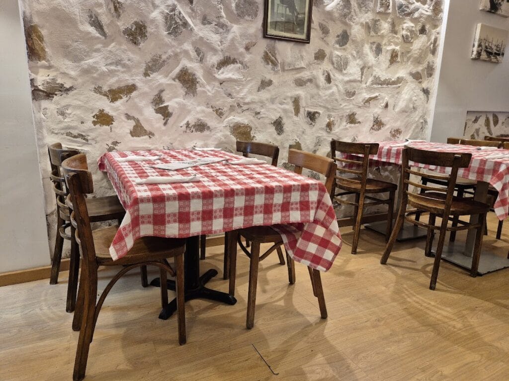 Interior de Pizzería Mamma Bohemia con mesas de manteles a cuadros rojos y blancos junto a pared de piedra rústica