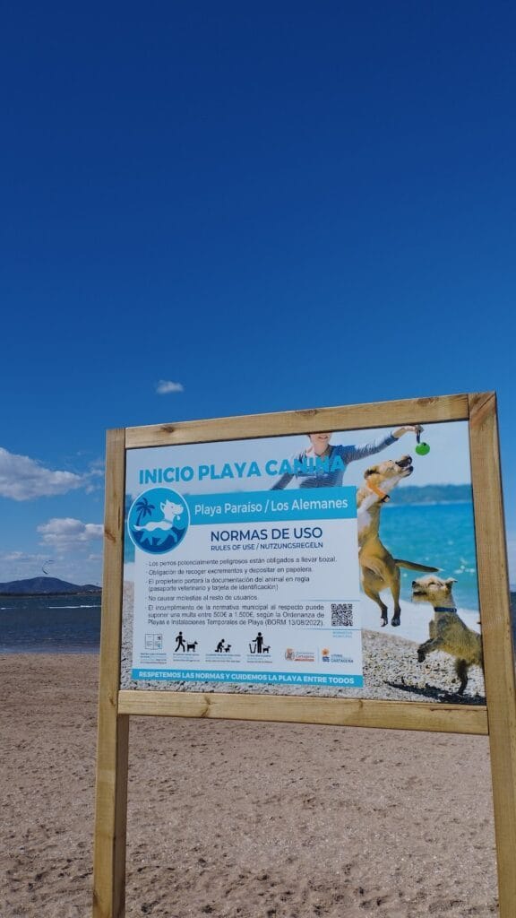 Cartel de inicio de la playa canina Playa Paraíso Los Alemanes con normas de uso y fotos de perros, con el Mar Menor al fondo en La Manga