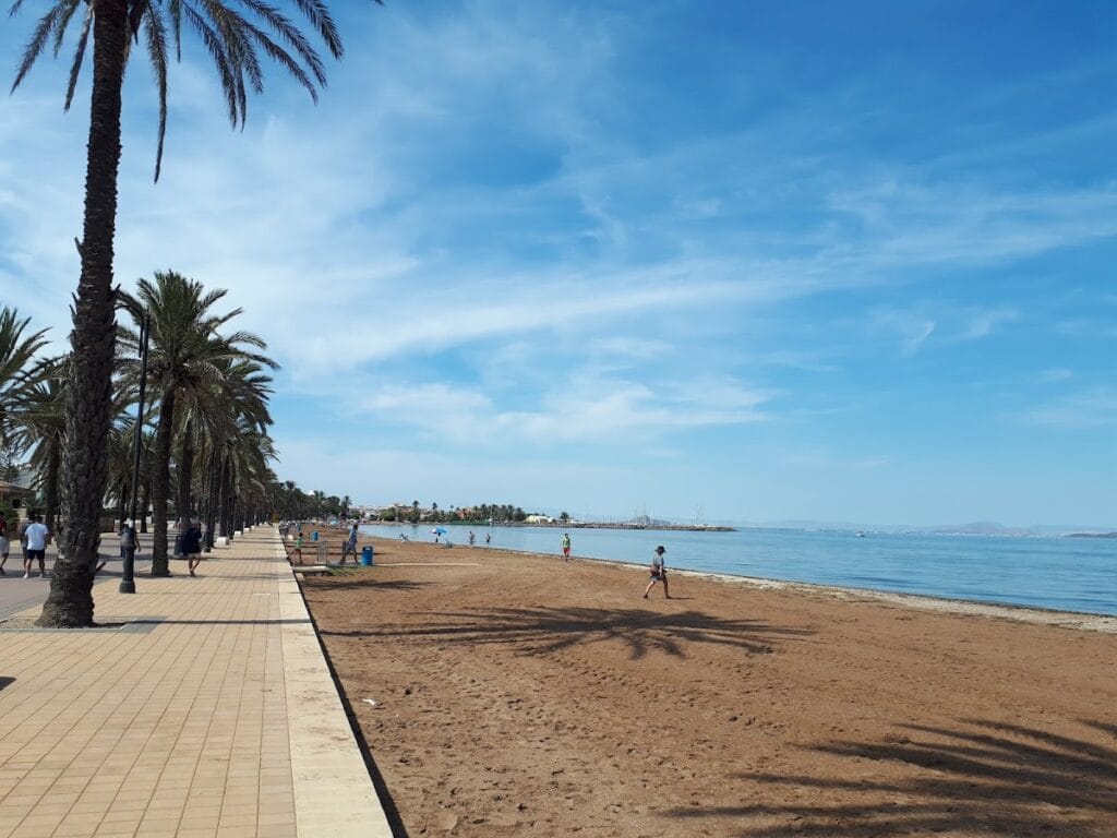 Paseo marítimo con palmeras junto a la arena y aguas tranquilas de la Playa de Mar de Cristal, La Manga del Mar Menor