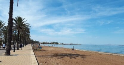 Paseo marítimo con palmeras junto a la arena y aguas tranquilas de la Playa de Mar de Cristal, La Manga del Mar Menor