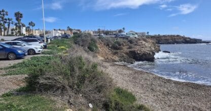 Costa rocosa de la Playa del Cura en Cabo de Palos con vegetación de matorral, pequeñas olas y aparcamiento al borde del acantilado
