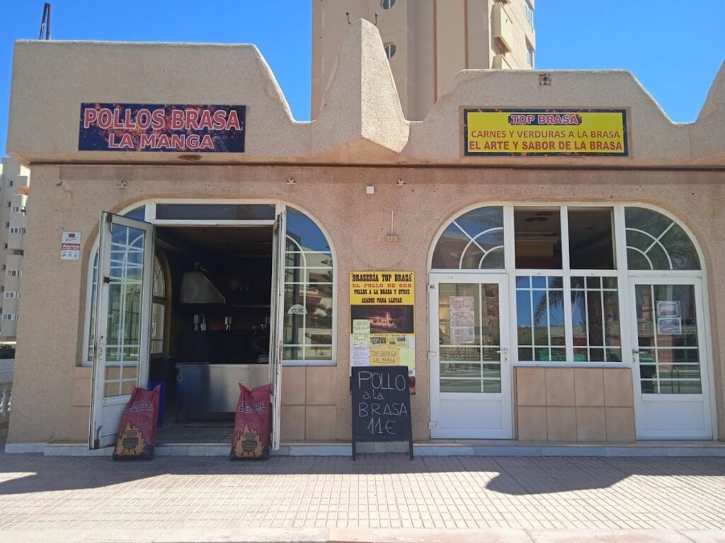 Fachada de Pollos Brasa La Manga con rótulos de brasería y cartel de pizarra anunciando pollo a la brasa para llevar