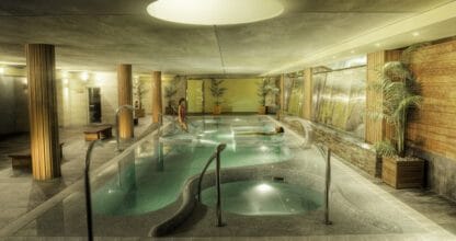 Zona de spa interior del Poseidon La Manga Hotel, piscina de hidromasaje con iluminación tenue, columnas de madera y dos personas relajándose