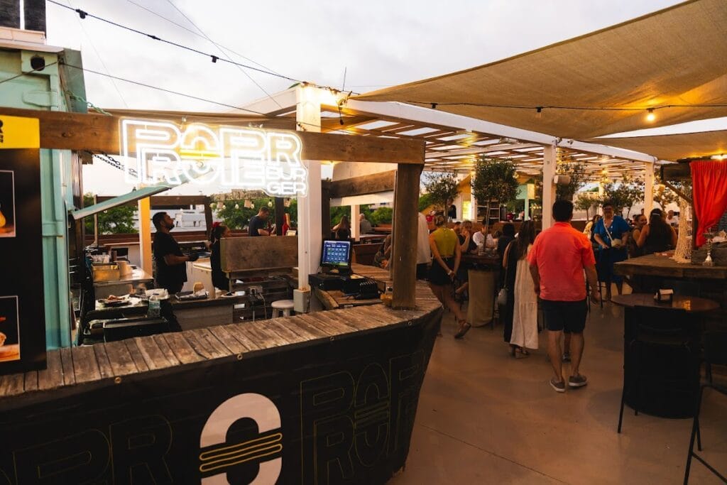 Puesto Proper Burger con cartel neón en la terraza del gastromercado La Fresca al atardecer, ambiente animado en La Manga