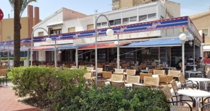 Terraza exterior del restaurante Ramón Sirvent en La Manga del Mar Menor, amplia zona con mesas y sillas bajo toldo azul y rojo