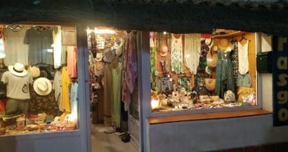 Tienda Rasgo con escaparates iluminados repletos de ropa, sombreros y complementos de playa en La Manga del Mar Menor