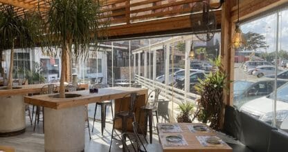 Interior luminoso del Restaurante Ándale La Manga con mesas de madera, taburetes metálicos y plantas tropicales