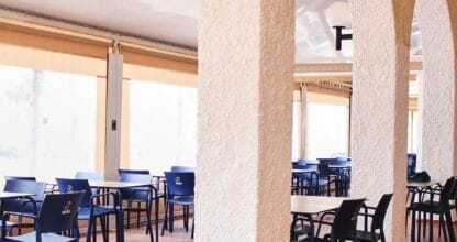 Comedor porticado del Restaurante El Murciano con arcos blancos de yeso, suelo de barro cocido y sillas azules, luz natural tamizada